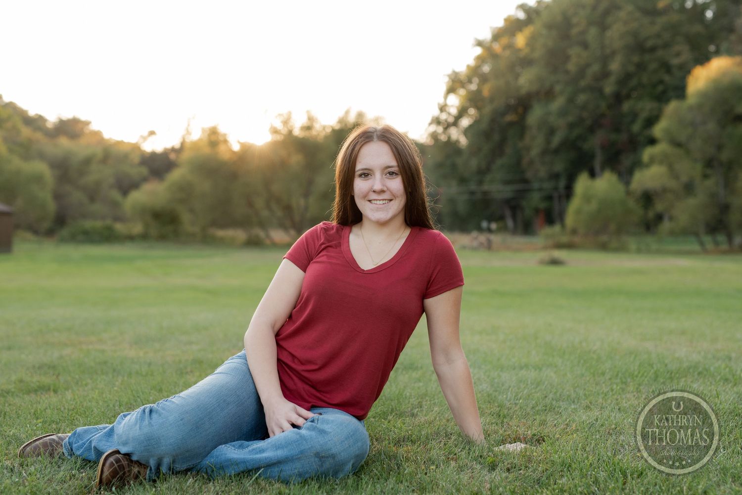 Someone relaxes on grass in a red v-neck shirt and jeans during a sunset photoshoot.