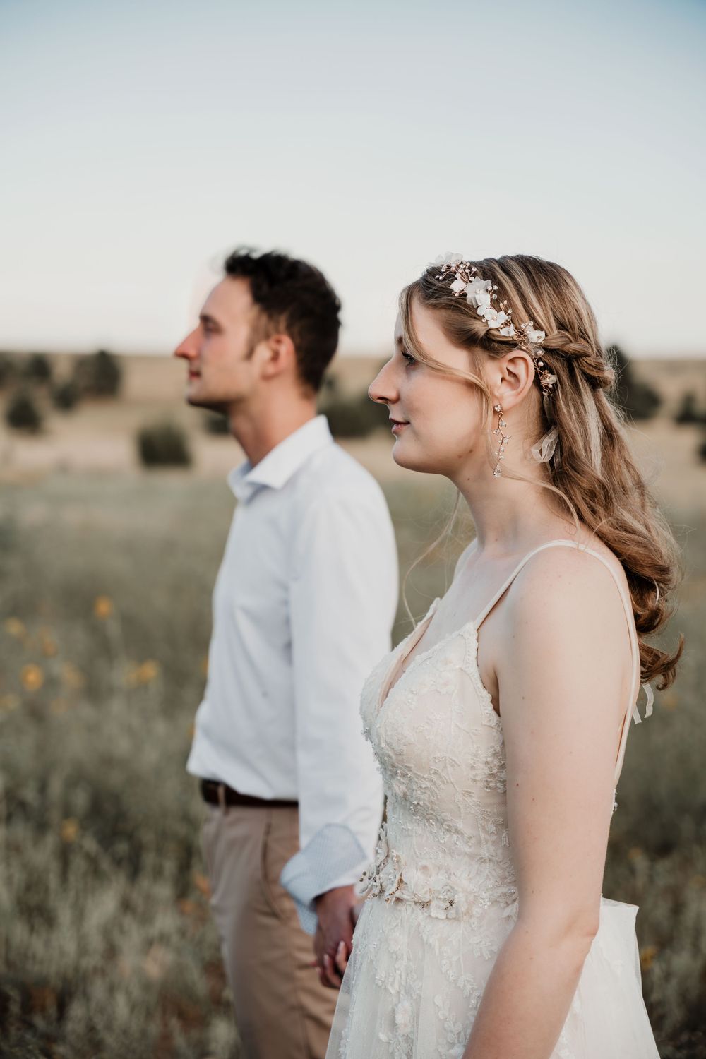 Candid side profile of couple in rustic field with delicate bridal details.