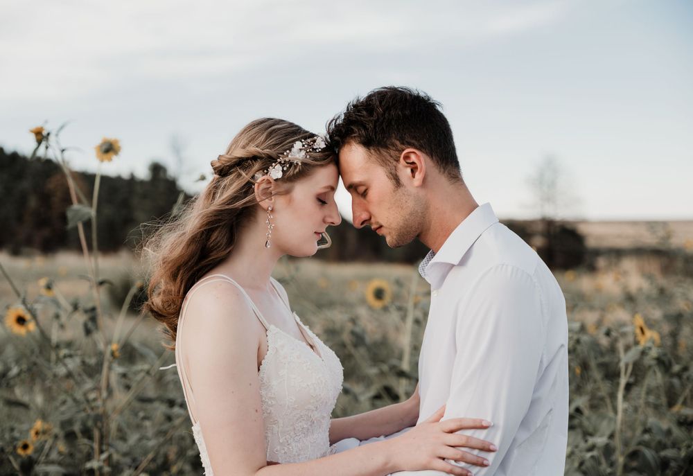 Intimate moment between couple in field of sunflowers during sunset photoshoot.