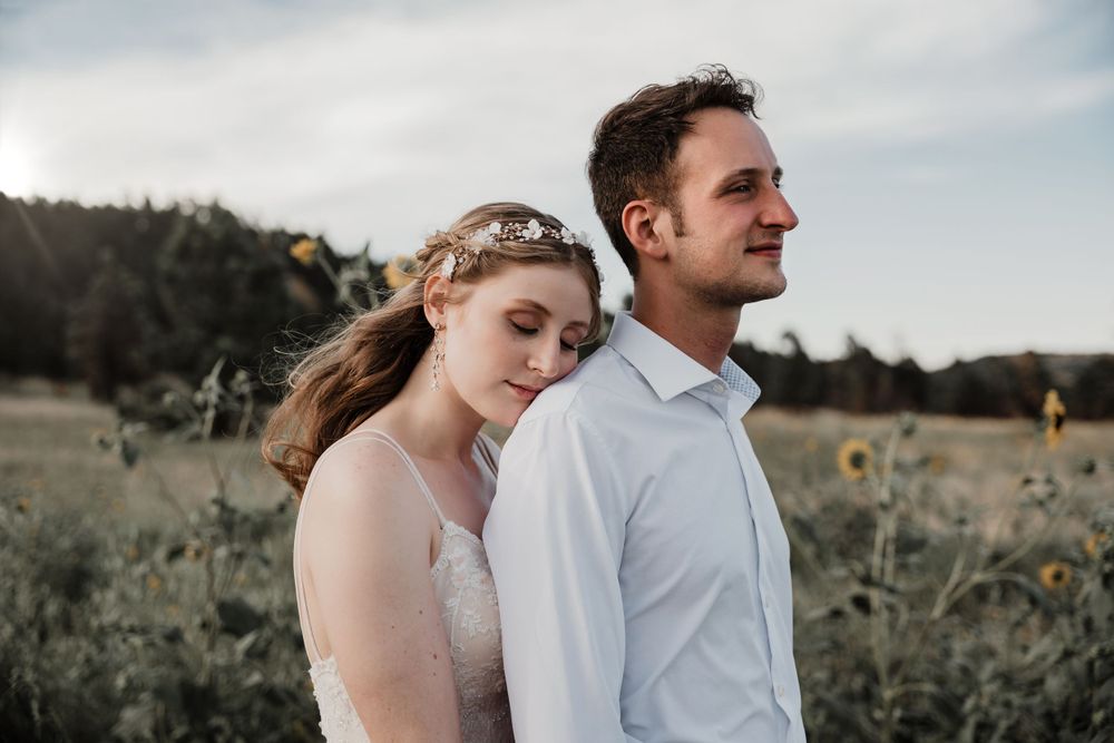 Romantic wedding couple stands in field of wildflowers at sunset with mountains in background.