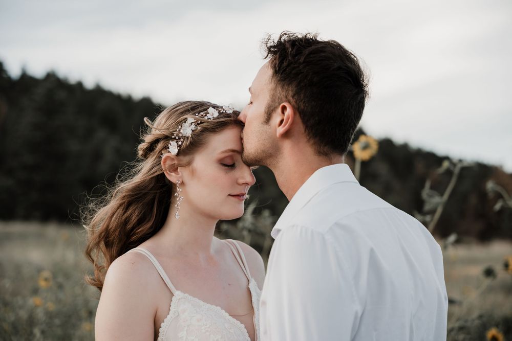 Gentle forehead kiss exchanged between couple in rustic outdoor setting.