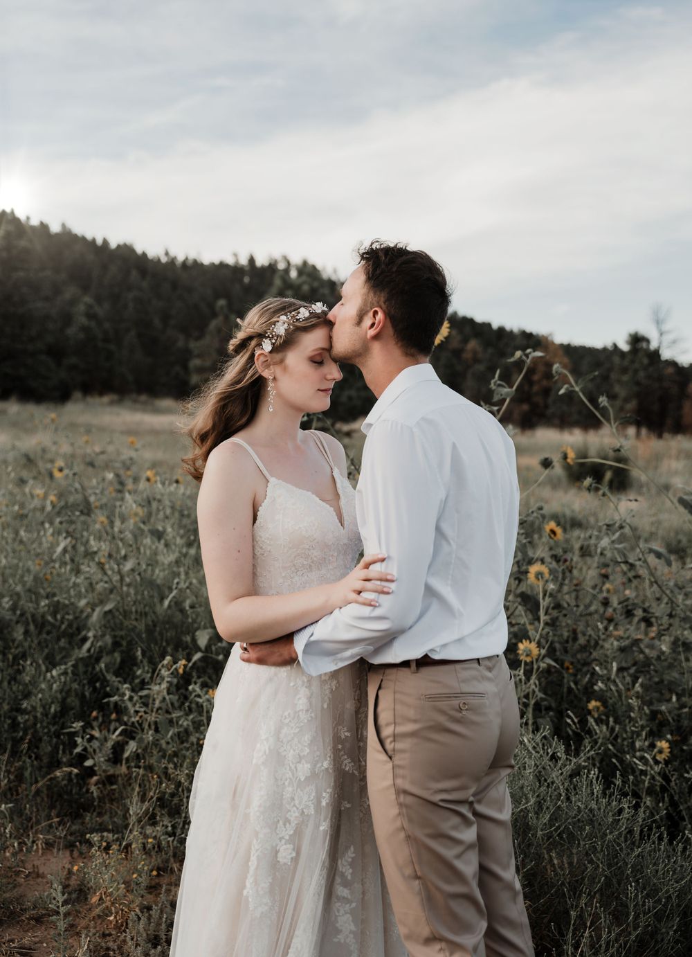 Intimate embrace between couple in field with mountains and cloudy sky backdrop.