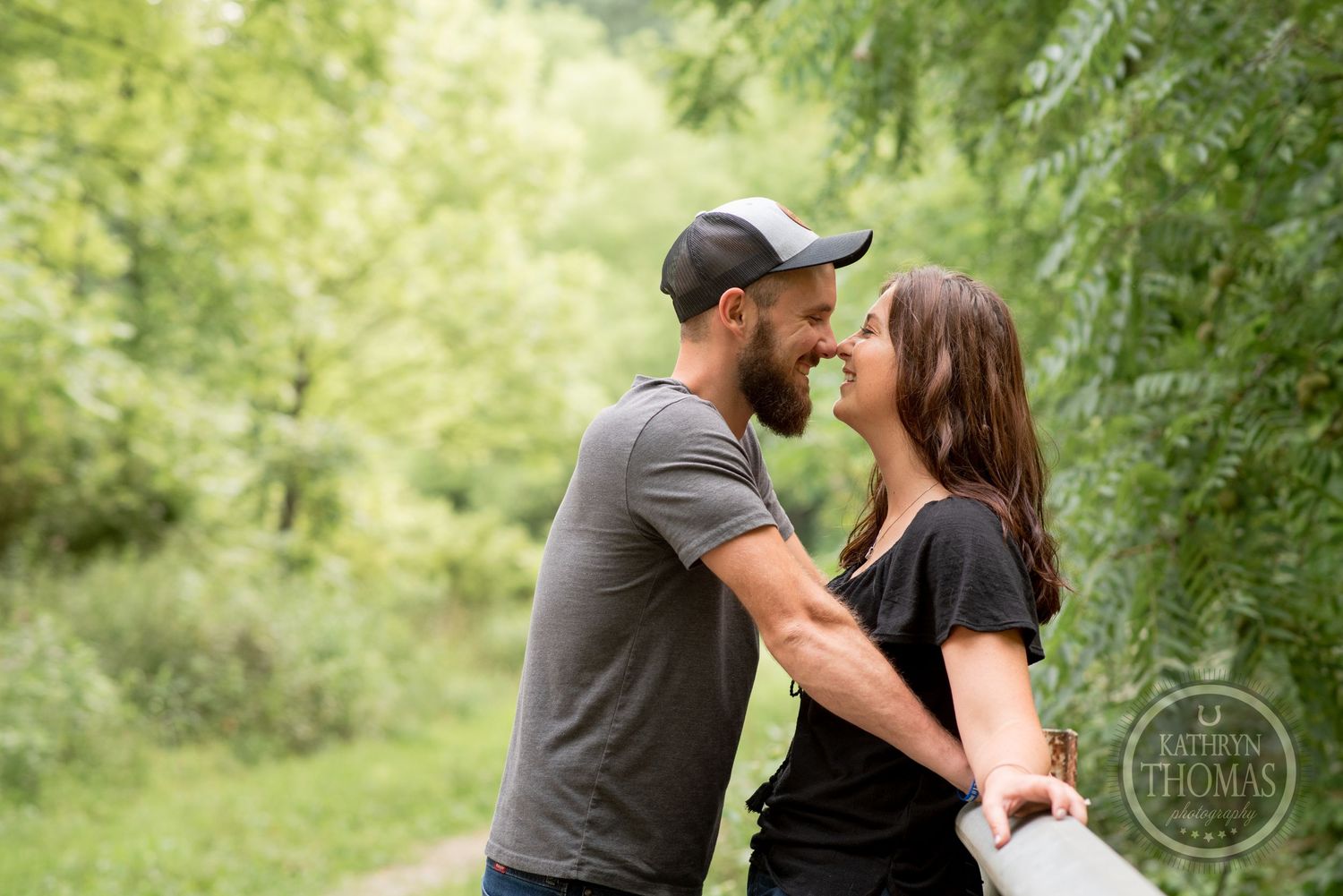 A romantic couple shares an intimate moment against a lush green forest backdrop.