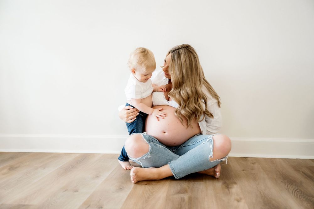 Family sitting together on hardwood floor in casual attire against white wall.