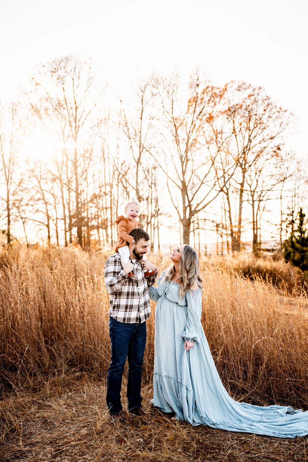 Couple in elegant attire embracing in rustic field at sunset.