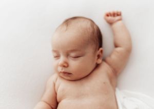 Sleeping baby with raised arm lying on soft white surface.