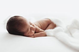 A peaceful sleeping newborn baby lying on soft white bedding in natural light.