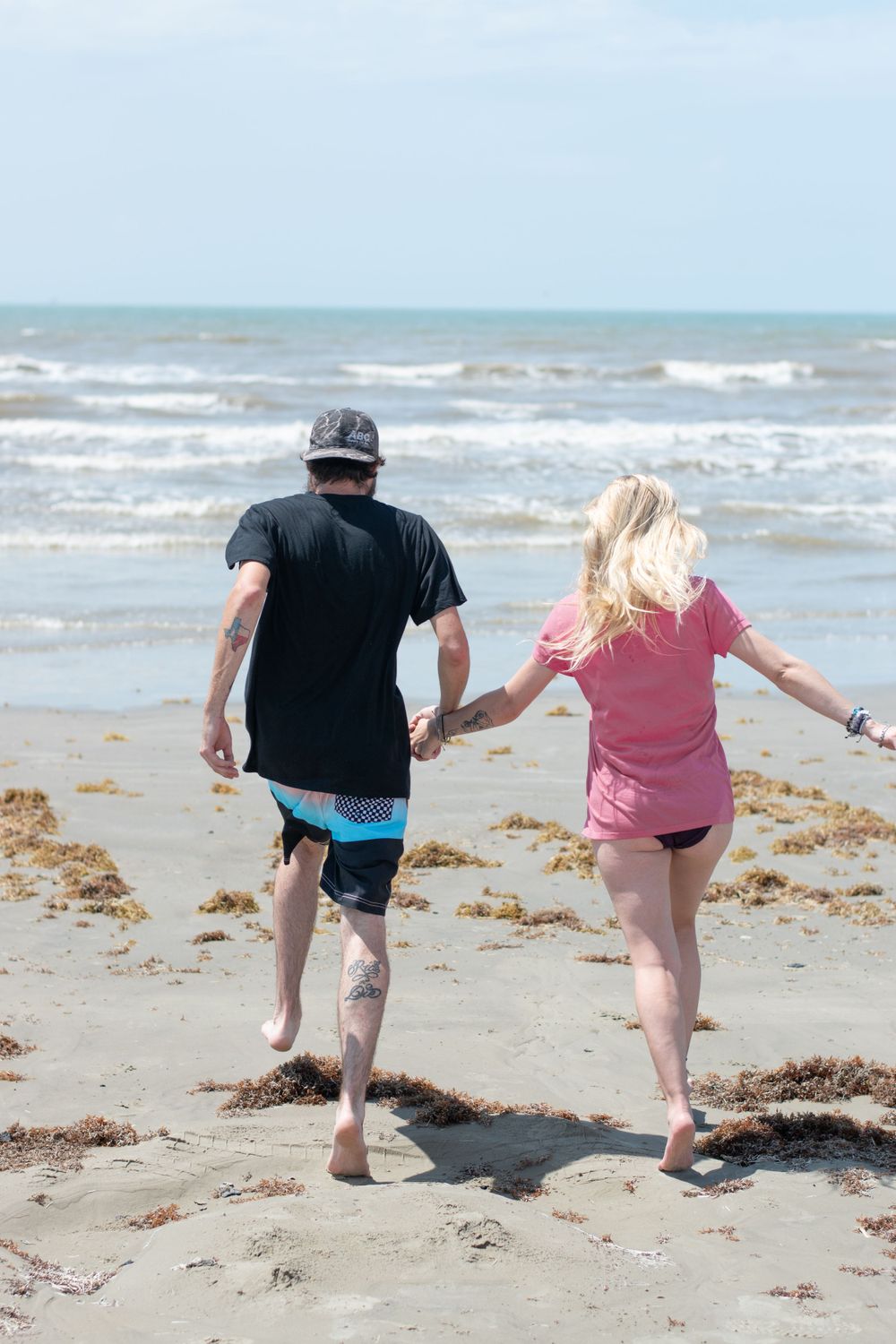 Couple walking hand in hand along shoreline at beach.