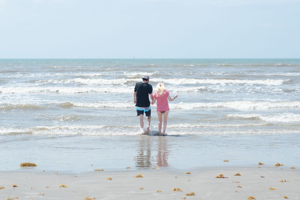 A couple stands together at the water's edge on a beach with gentle waves rolling in.