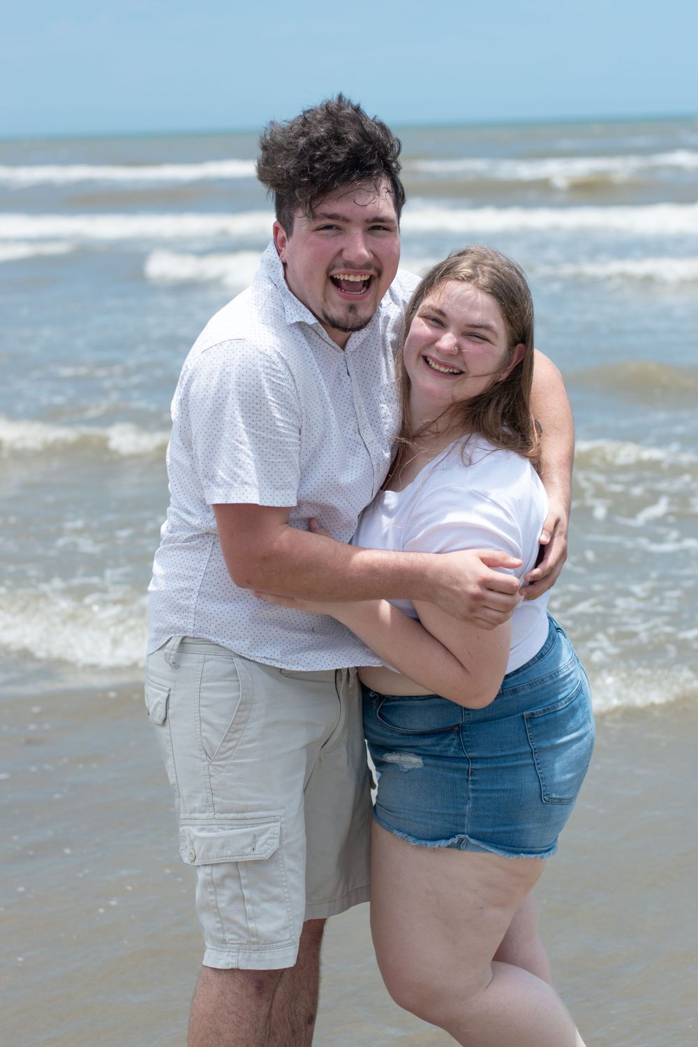 A joyful couple laughs together while embracing on a sunny beach.