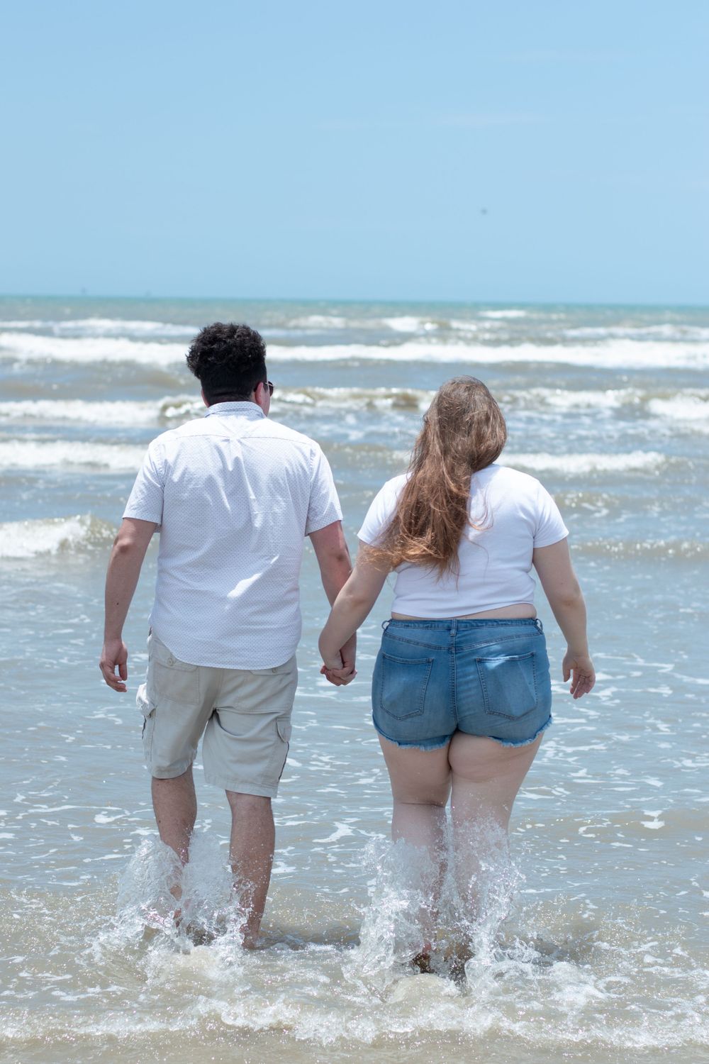 Couple holding hands while walking together in the shallow ocean waves.