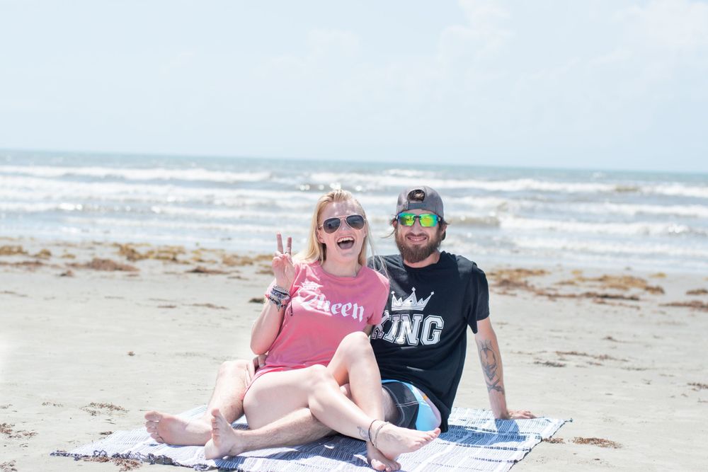 Couple in casual beachwear poses together on blanket by ocean.