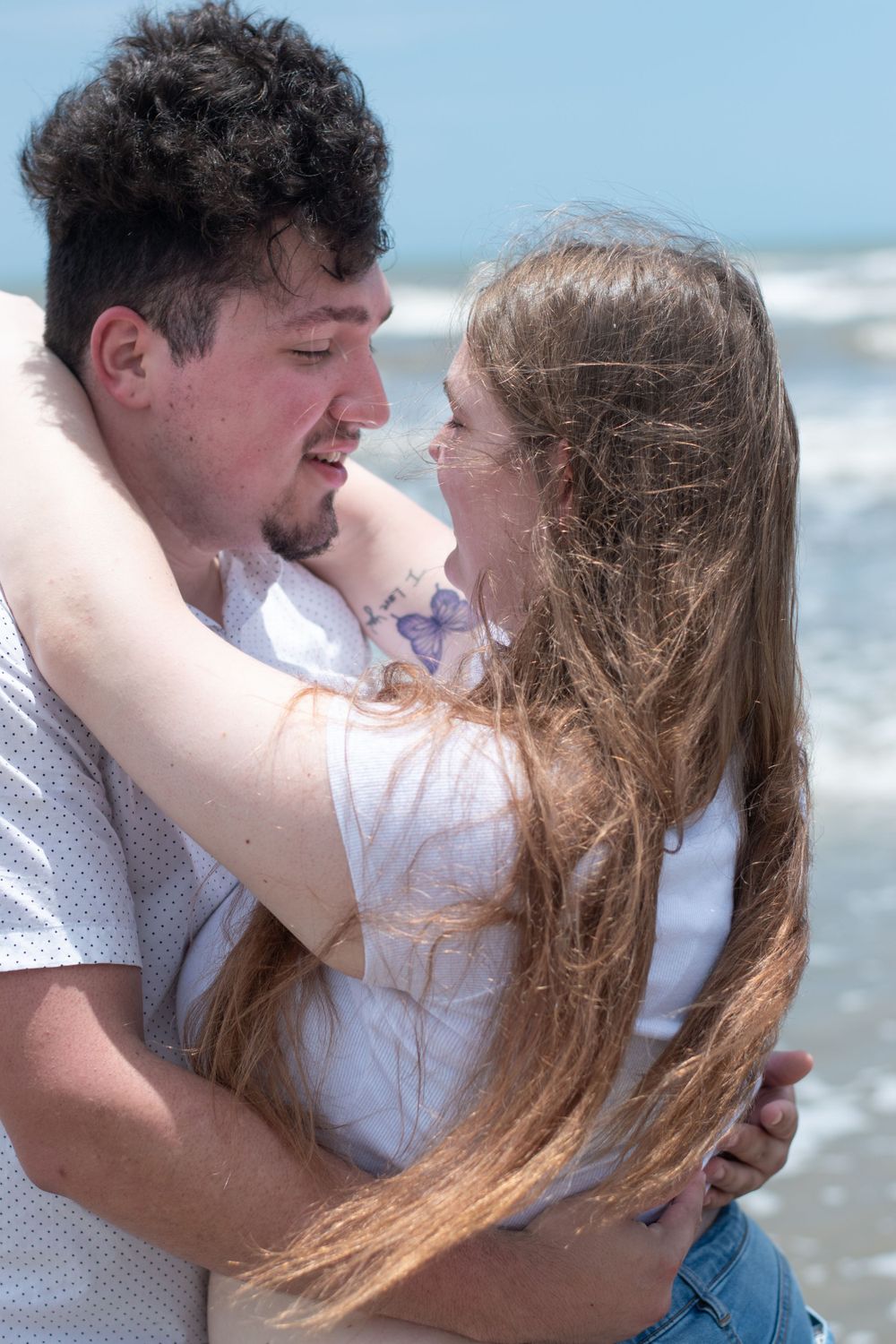 A loving couple shares an intimate moment on the beach with waves crashing behind them.