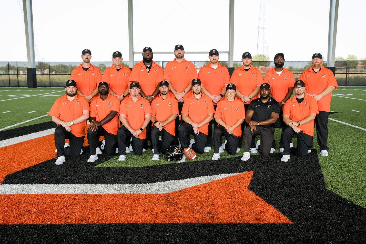 Sports team in matching orange uniforms posed for group photo on turf field.