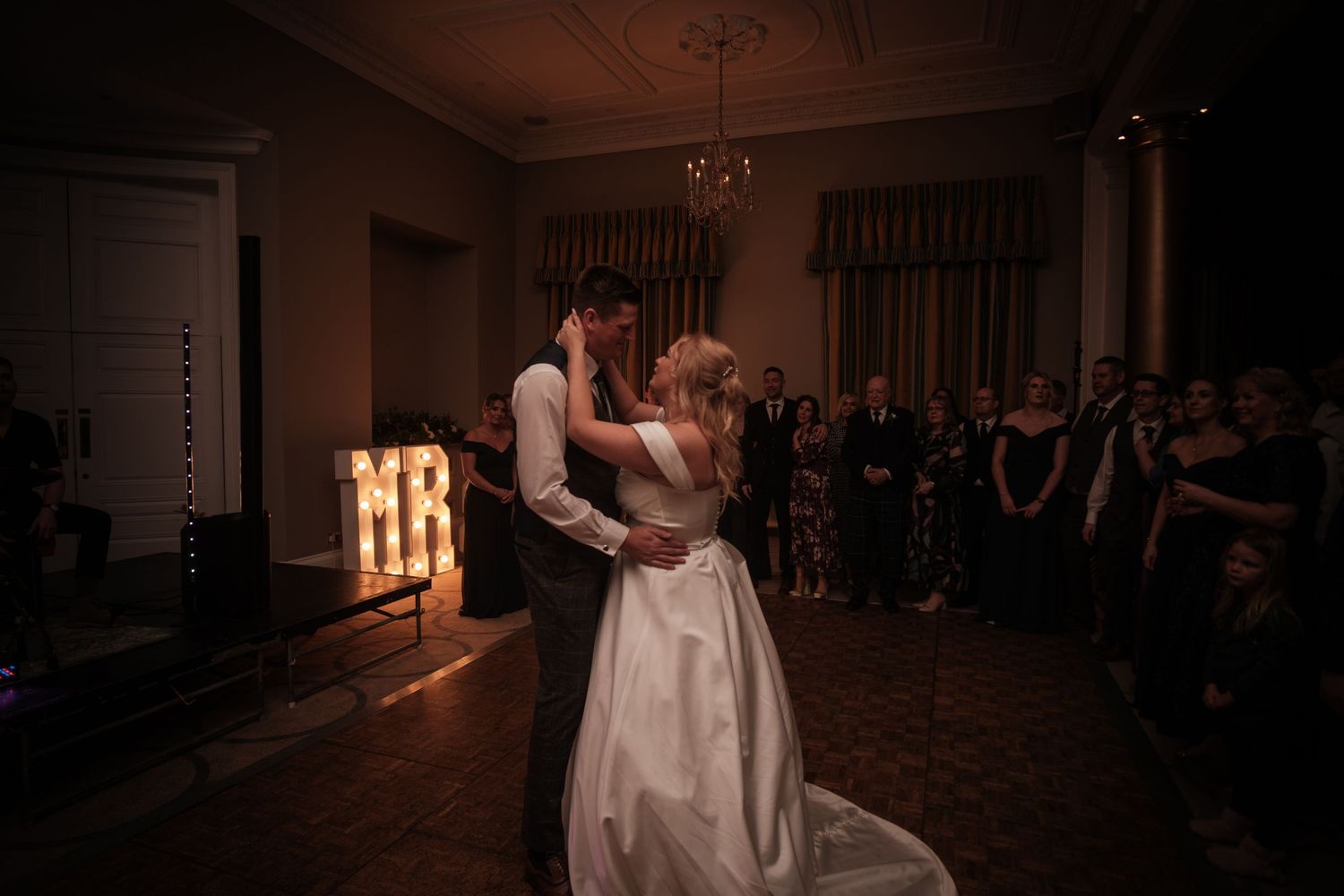 A first dance moment in an elegant ballroom with illuminated 'MR' letters in the background.