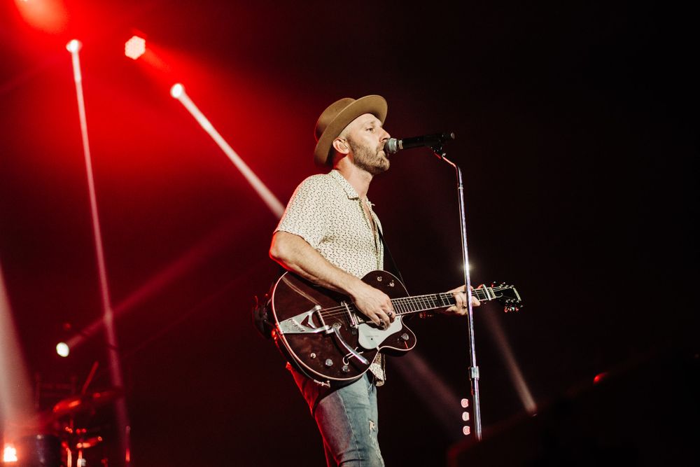 Musician performing on stage with guitar under dramatic red spotlights.