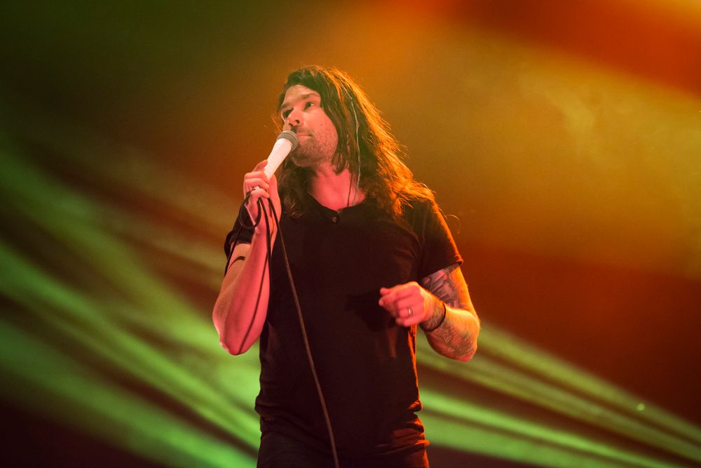 Passionate vocal performance on stage with dramatic orange and green lighting effects.