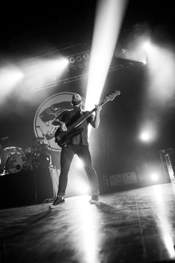 A guitarist performs on stage in dramatic black and white lighting during a concert performance.