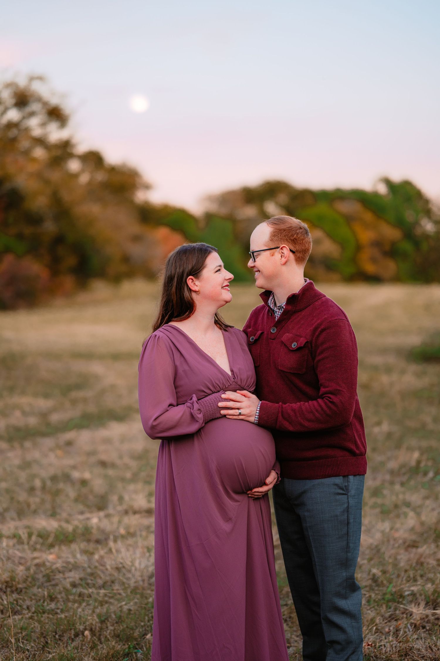 Mom and Dad looking each other while holding baby bump during outdoor Dallas area maternity photo session at sunset