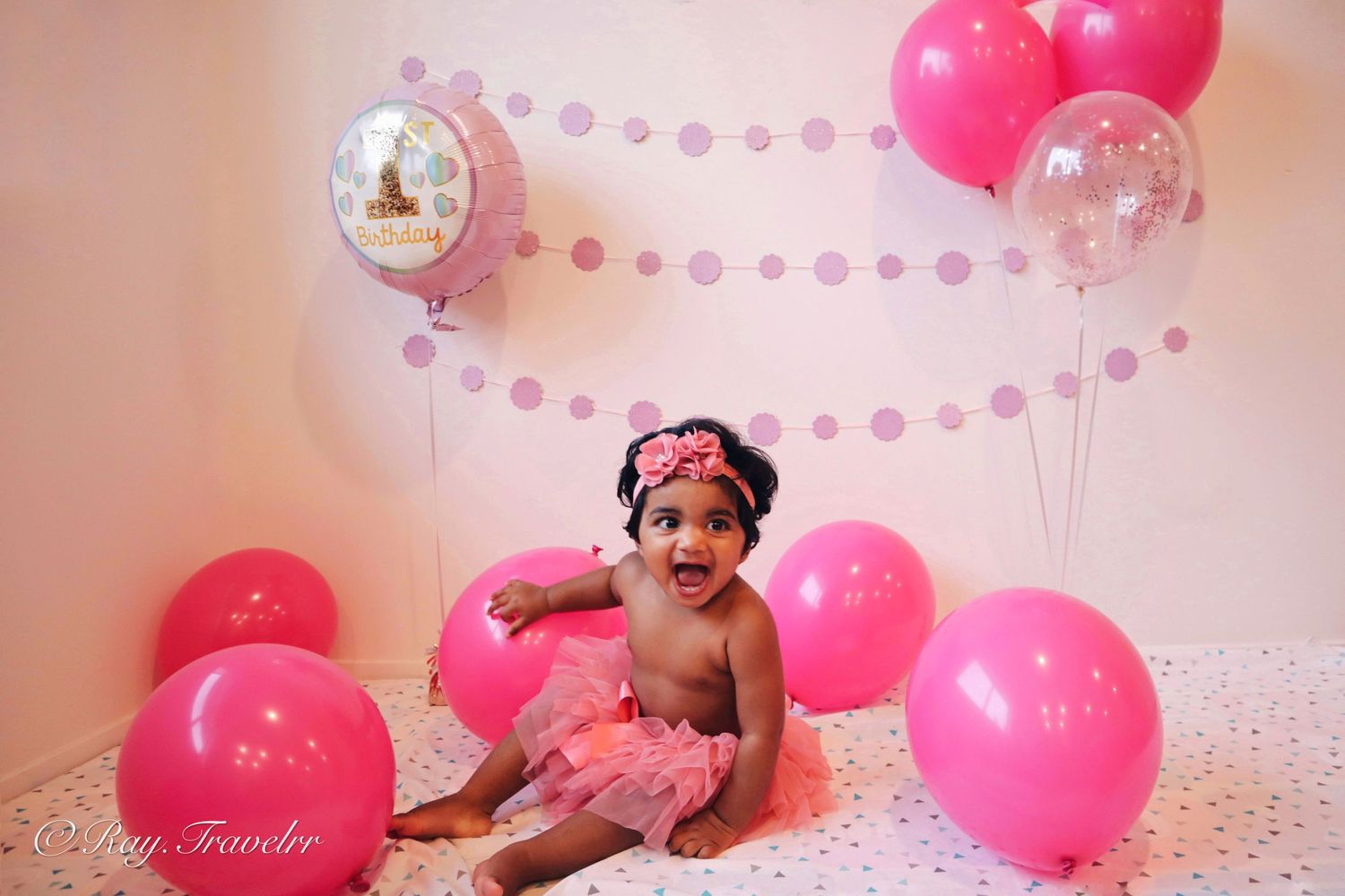 Baby birthday photo setup with pink balloons and pearl garland decorations.