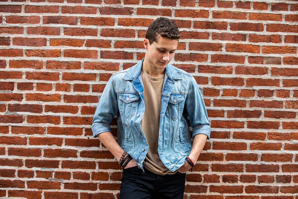 Person in denim jacket smiling against red brick wall background.