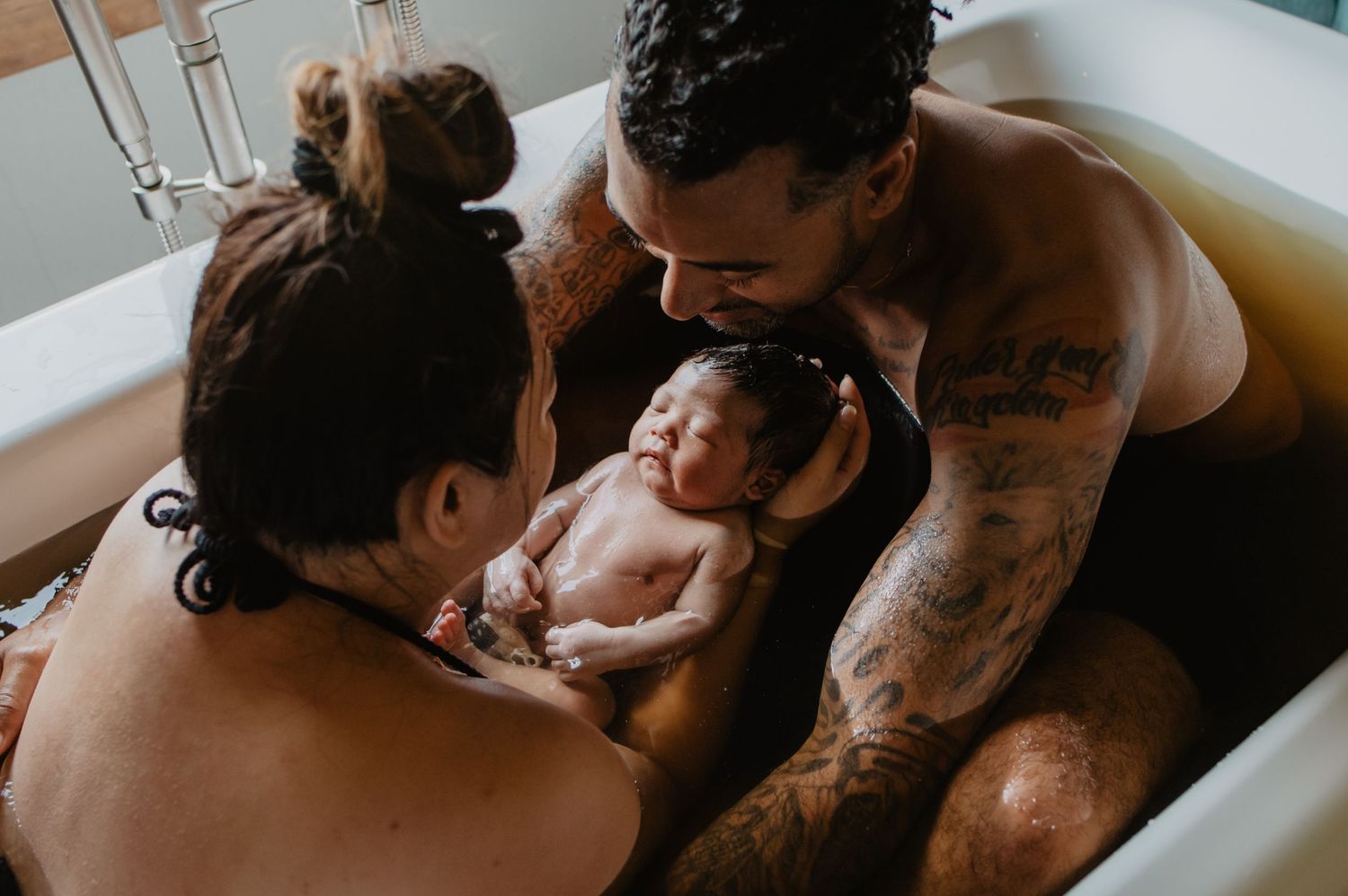 man and wife holding baby in an herbal bath at the birth center, immediately after giving birth