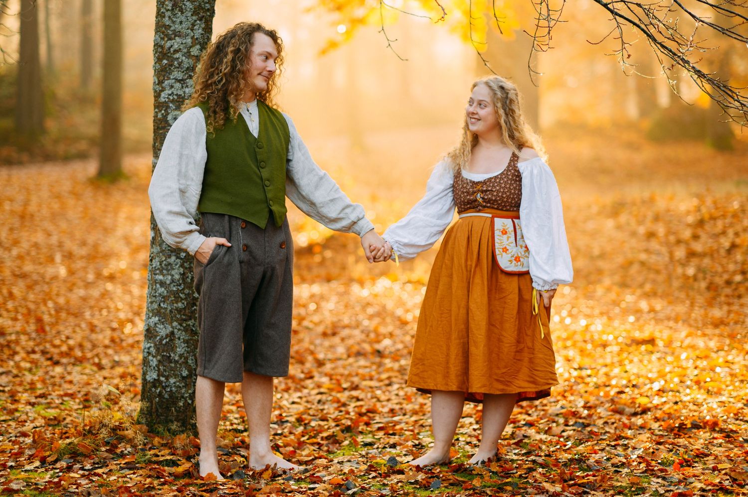 Couple in Renaissance costumes holding hands in autumn forest with golden leaves.