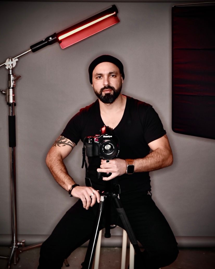 Photographer in black attire working with camera equipment in studio setting.