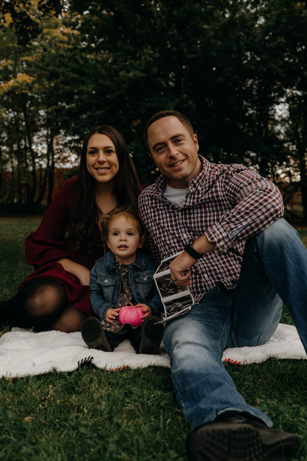 Family relaxing on blanket outdoors holding ultrasound photos.