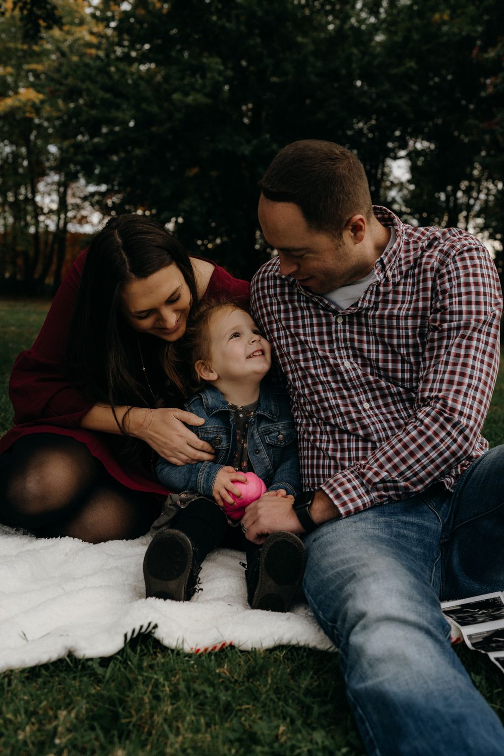 Family sitting together on white blanket outdoors sharing joyful moment.