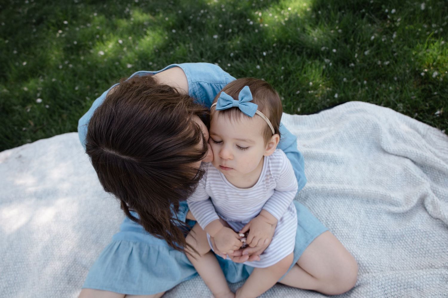Sioux City, Iowa photographer. Mother tenderly kissing baby on blanket outdoors in green garden setting.