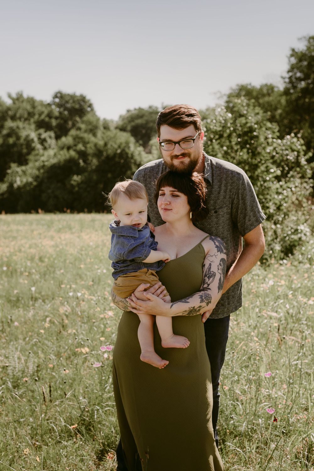 A tender family portrait in a flowering meadow with natural sunlight filtering through trees.