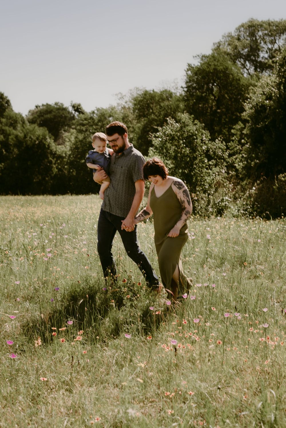 A family walks together through tall grass in a sun-filled meadow.