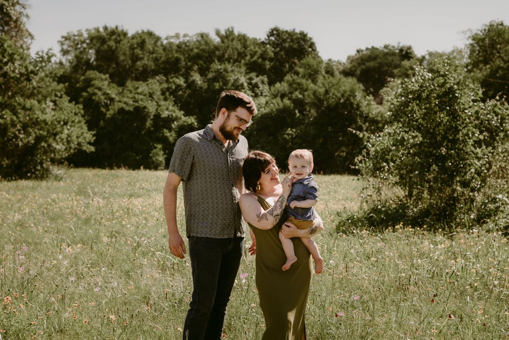 A family stands together in a sunlit meadow surrounded by green trees on a warm summer day.