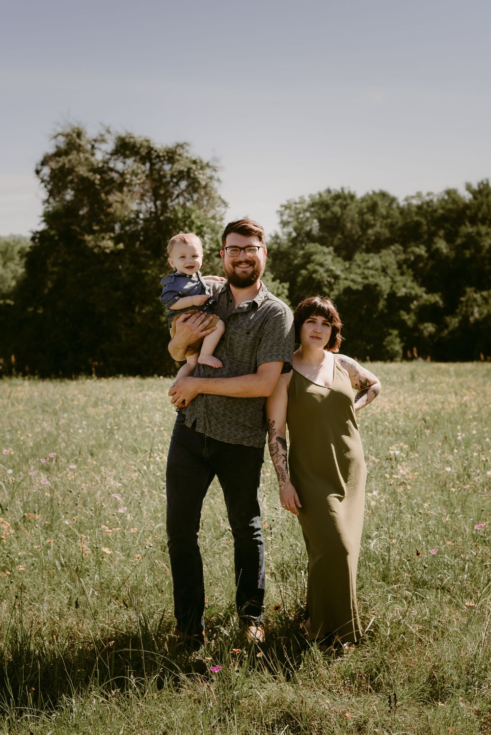 A family poses together in a golden meadow during sunset with trees in the background.