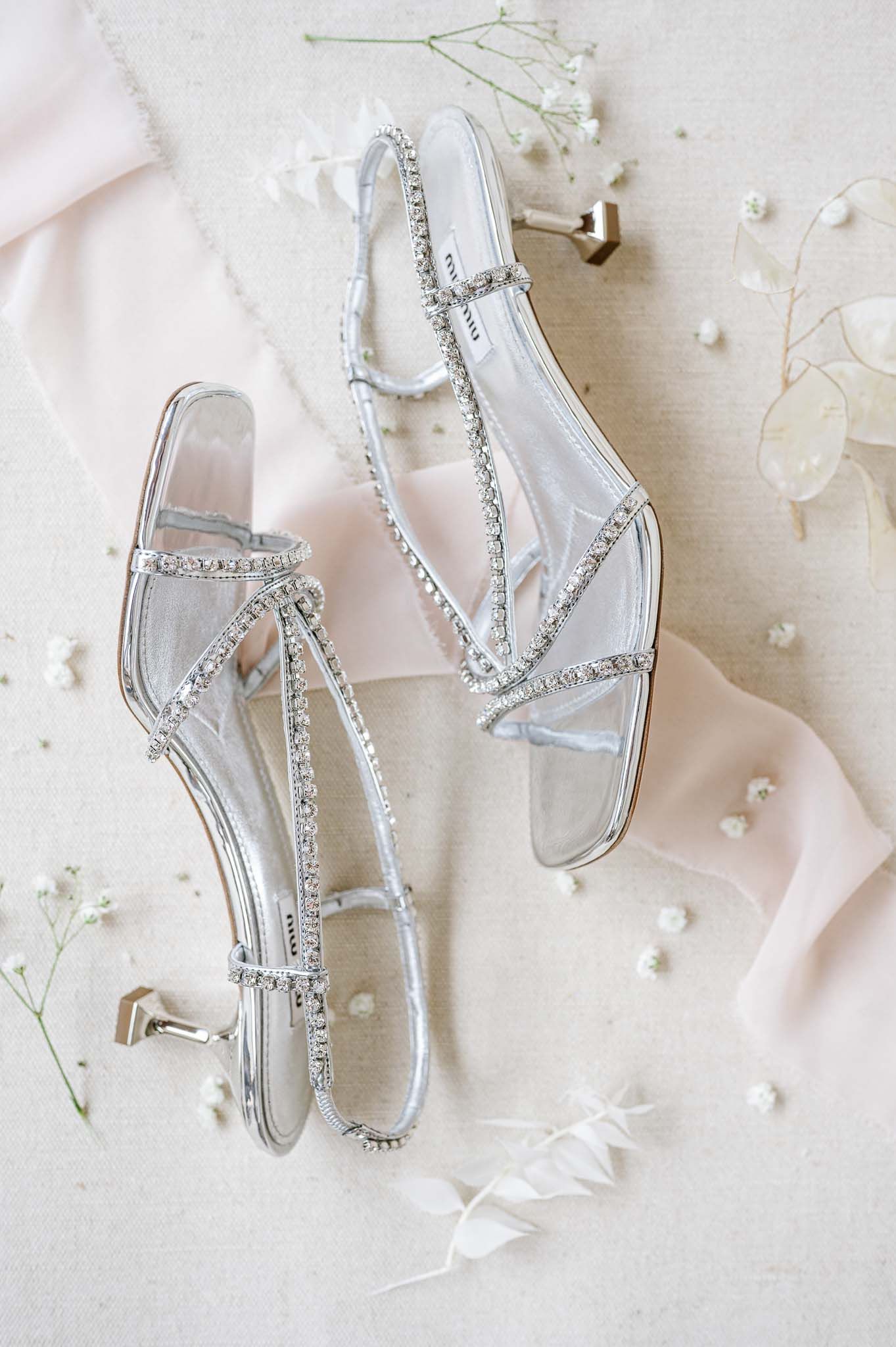 Crystal-embellished flat sandals styled with delicate flowers and feathers on neutral background.