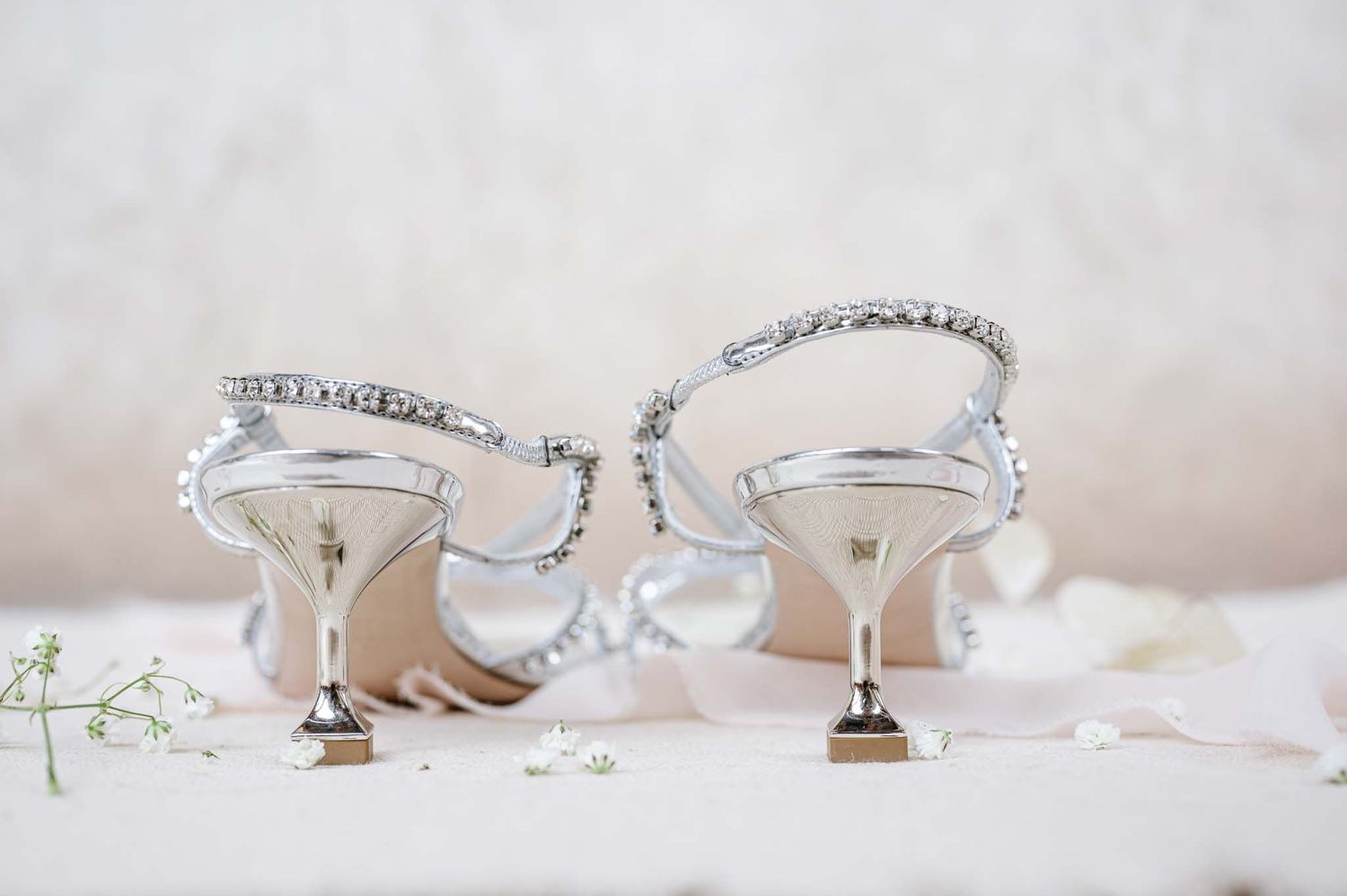 Elegant silver bridal shoes with crystal embellishments on light background.