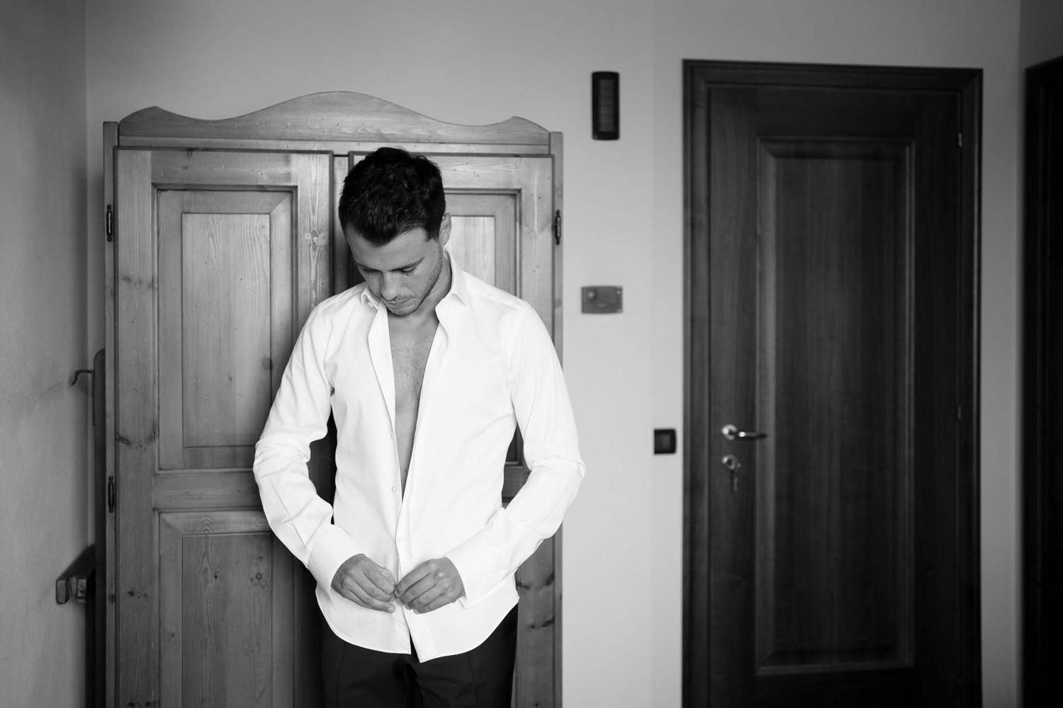 Black and white photo of person buttoning up white shirt while getting ready.