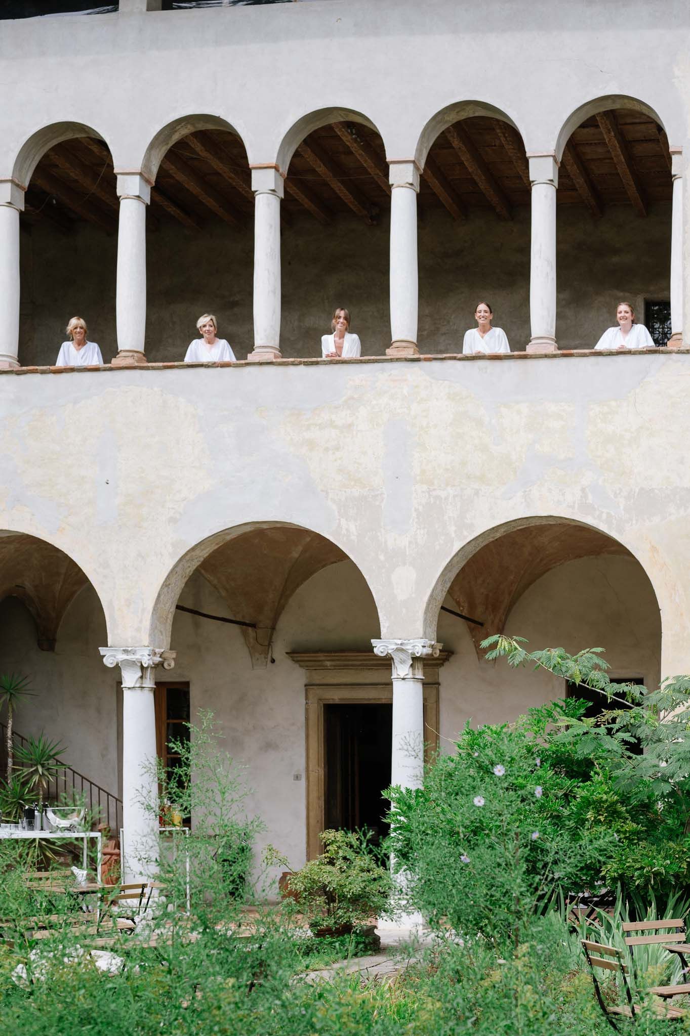 Figures in white clothing stand along an arched colonnade of a historic Mediterranean building.