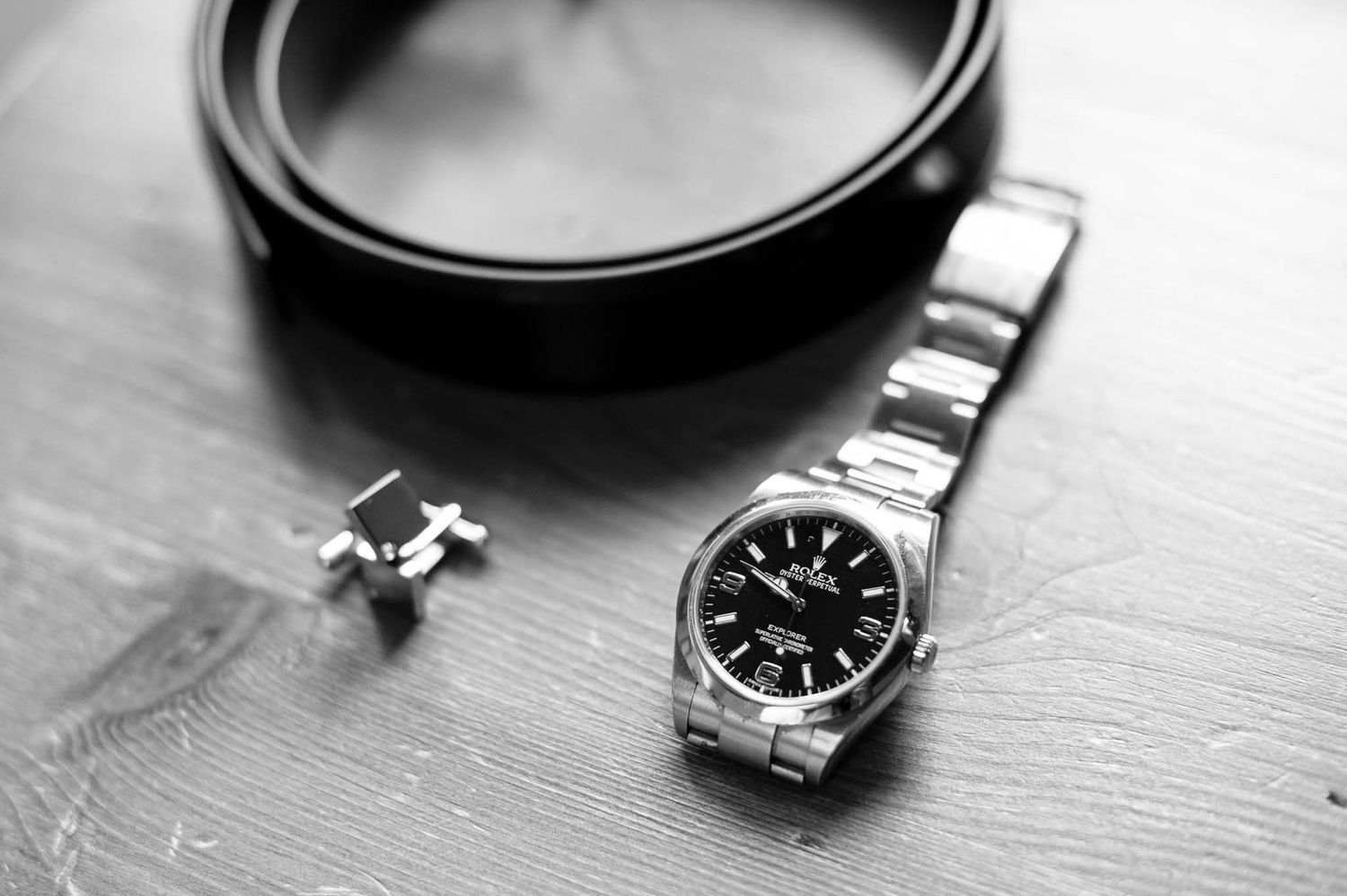 A silver watch and cufflinks arranged on a wooden surface in black and white.