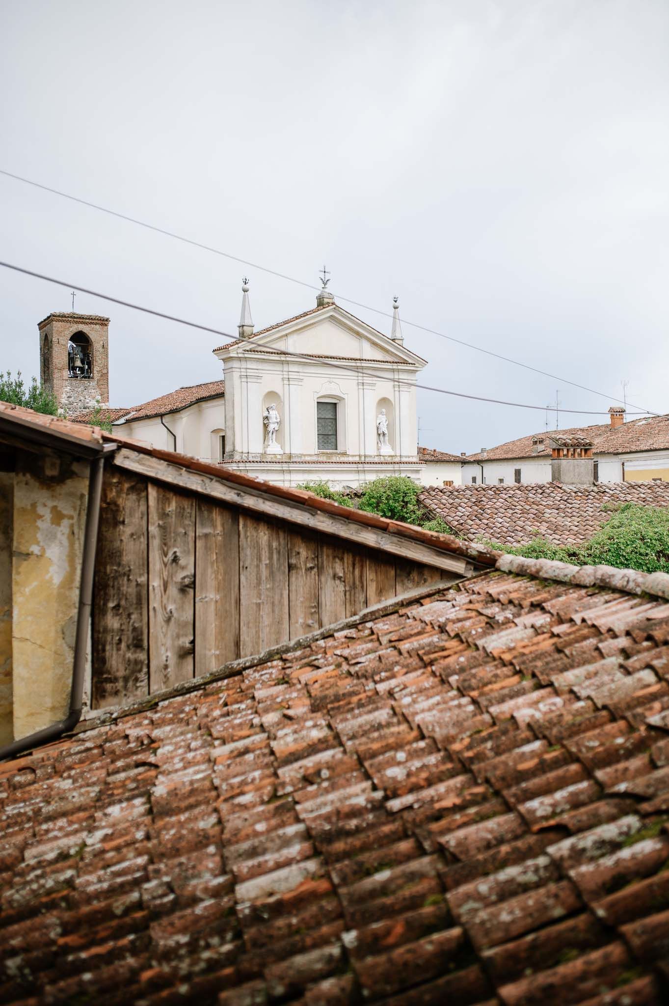 Church facade with bell tower visible over terracotta rooftops in an Italian village.