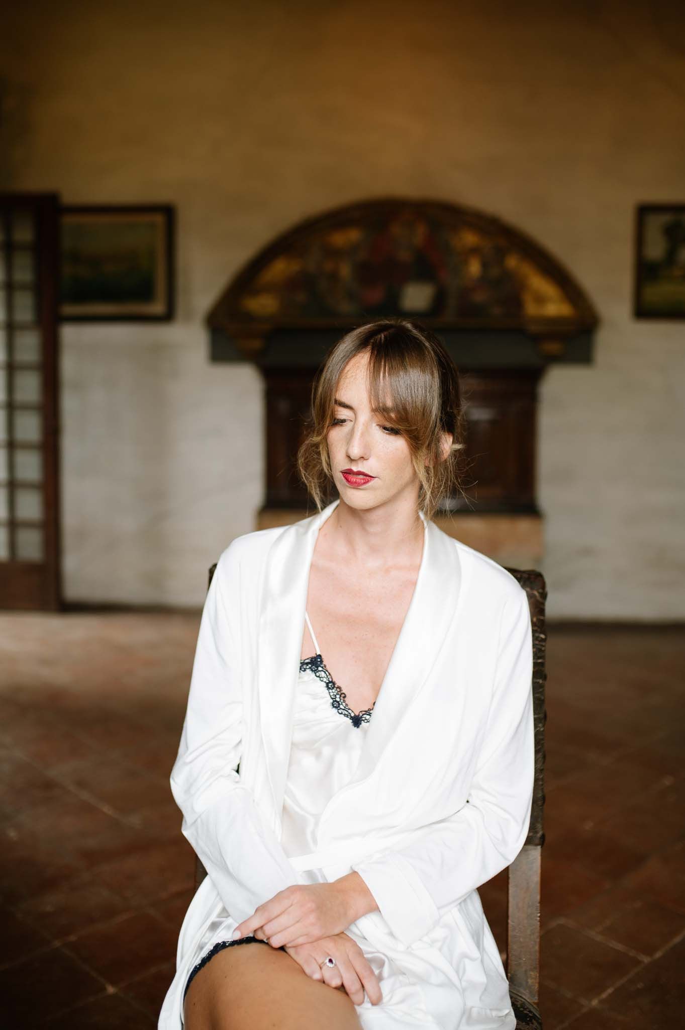 A figure in a white robe poses elegantly in a historic interior setting.