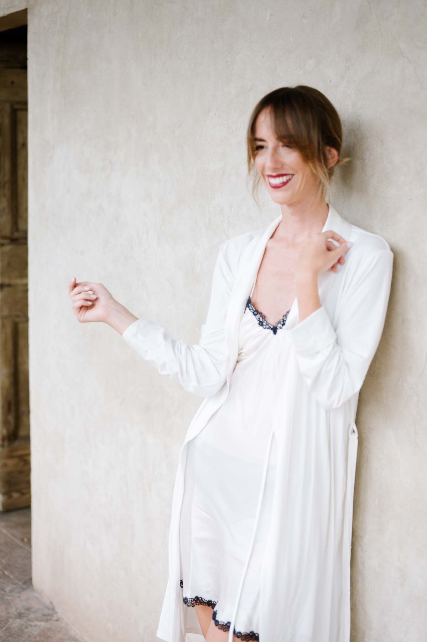 A figure in white attire poses playfully against a neutral wall.