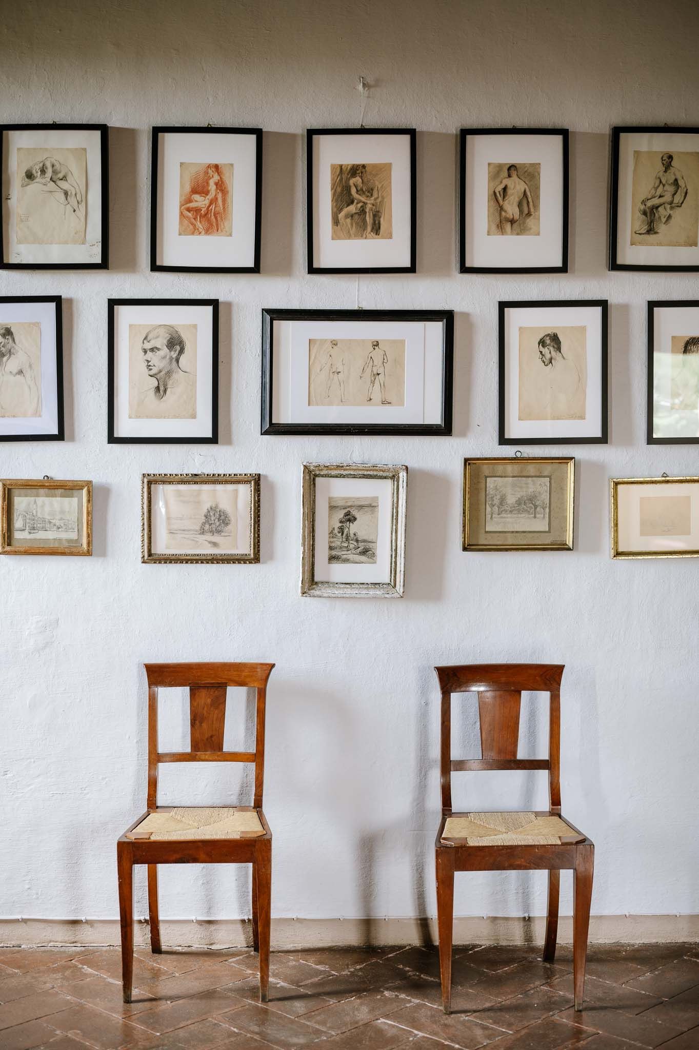 Two wooden chairs beneath a gallery wall of framed vintage sketches and portraits.