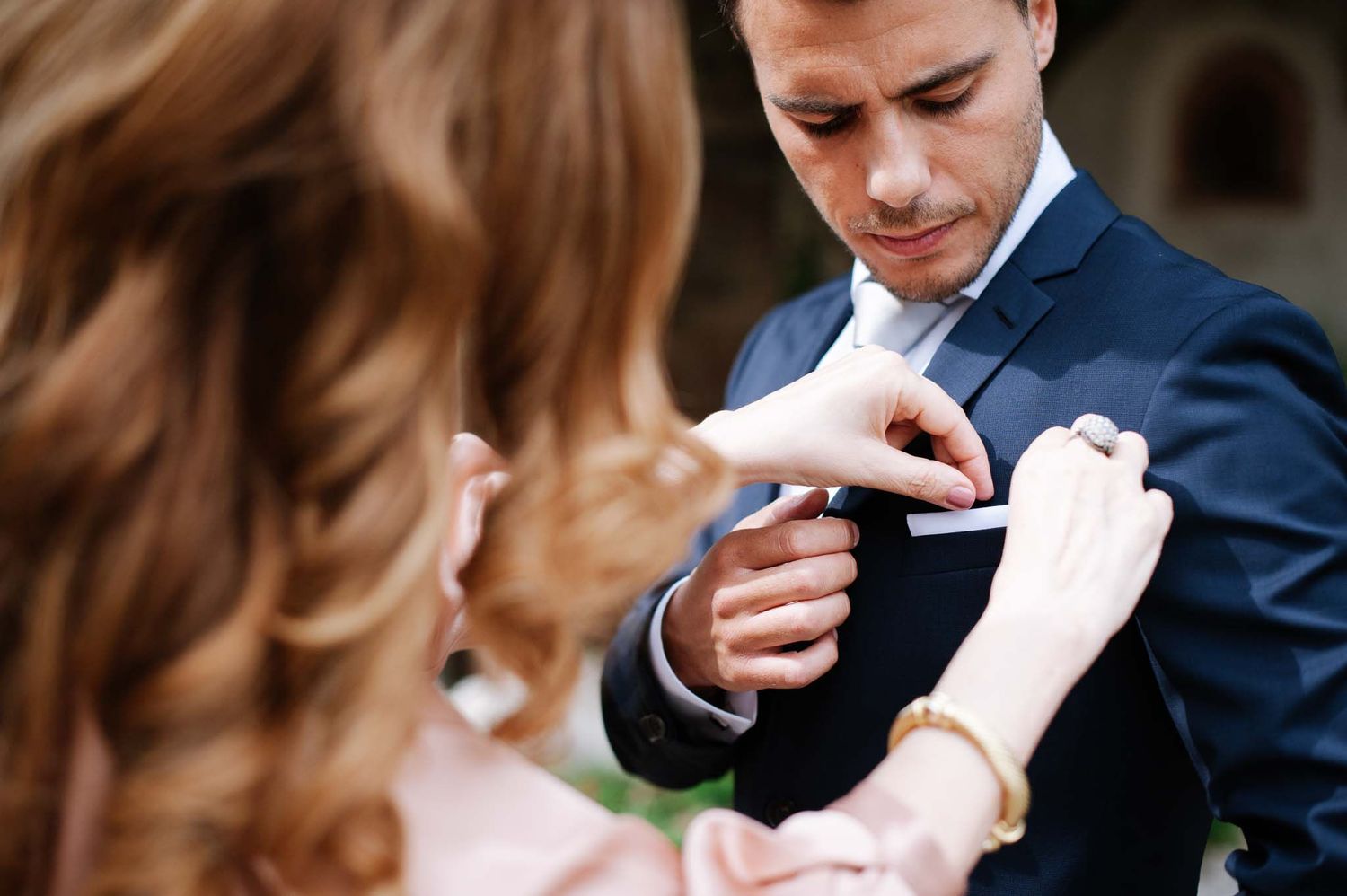 A closeup of hands adjusting formal attire during an intimate outdoor moment.