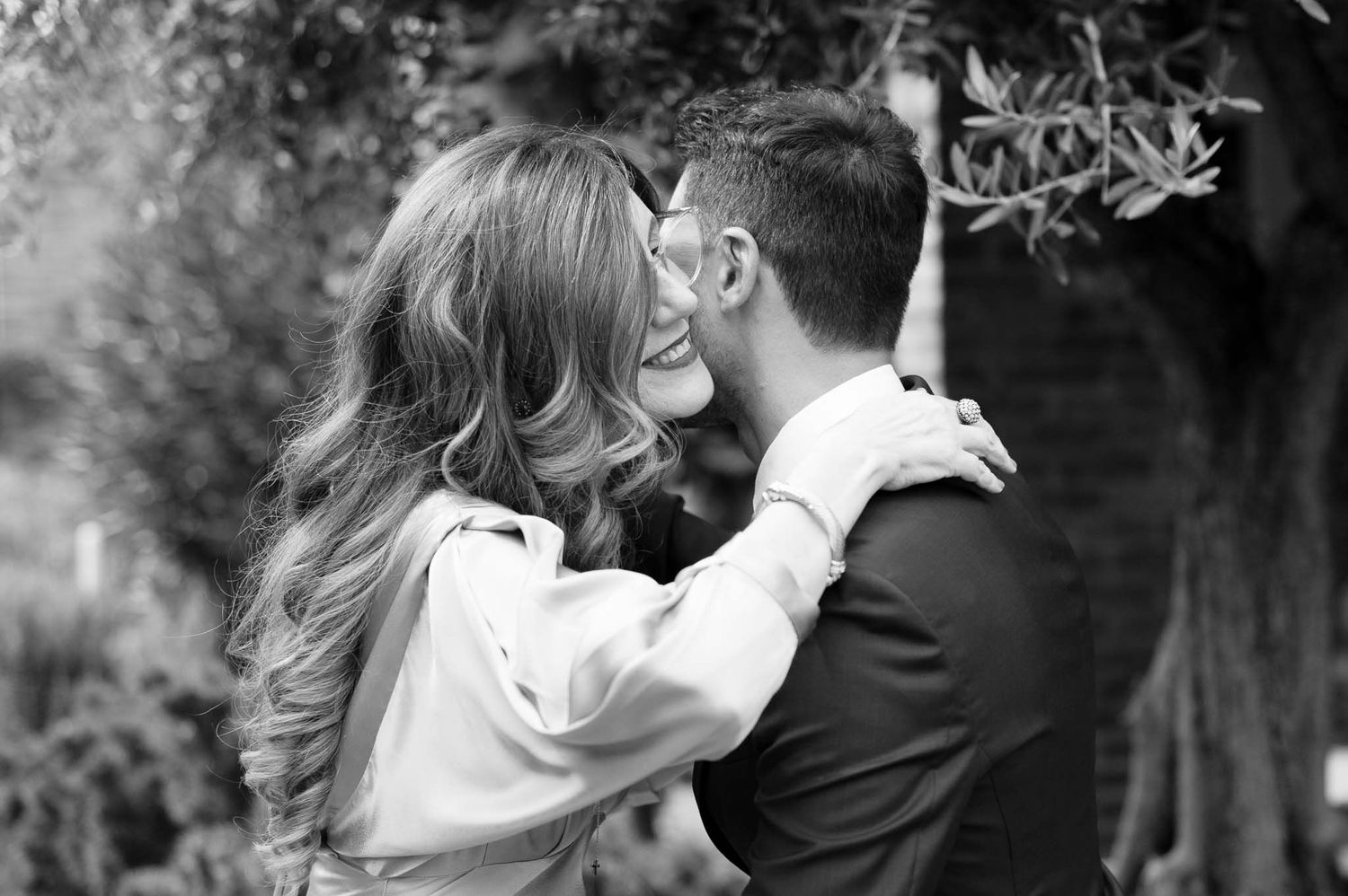 Black and white romantic moment of a couple sharing an intimate kiss outdoors in a garden setting.