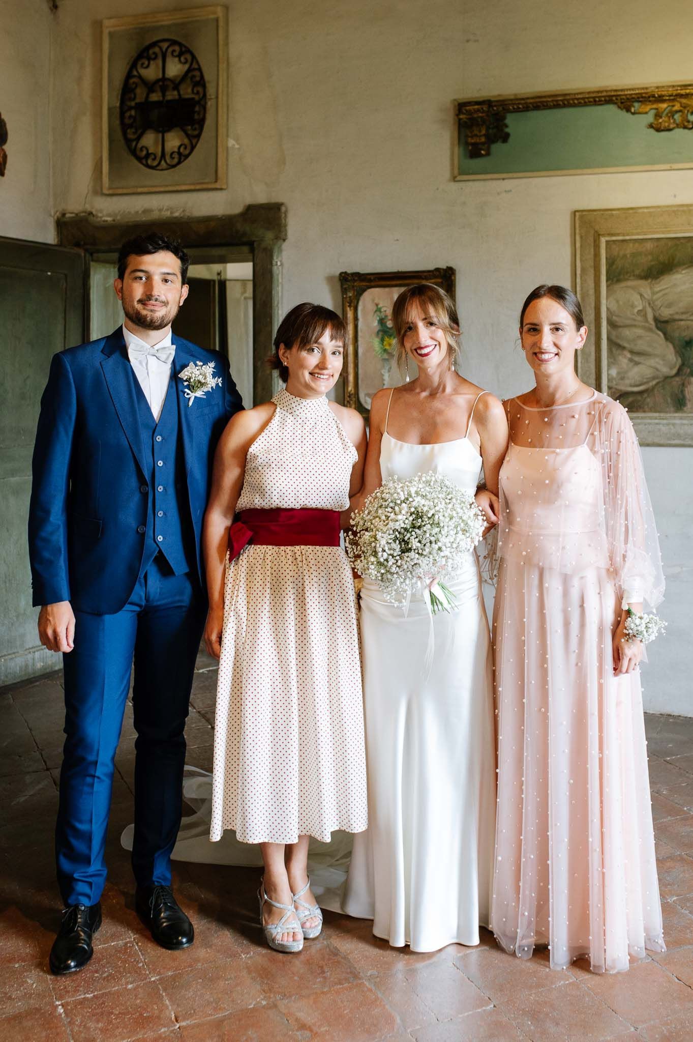 Wedding party poses in a historic hallway with blush dresses and navy suit holding baby's breath bouquets.