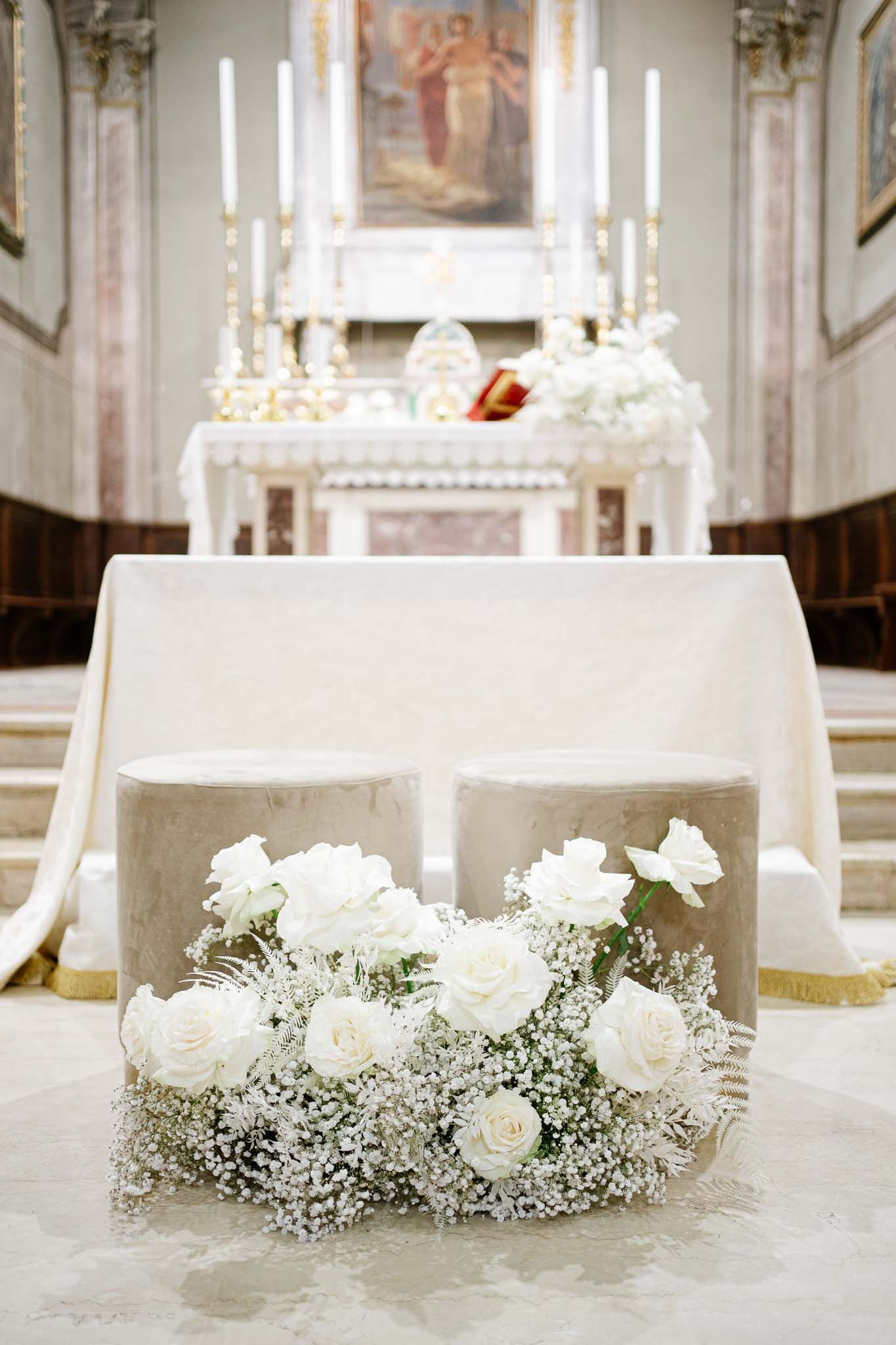 White roses and baby's breath flower arrangement on church altar with white candles and religious artwork.