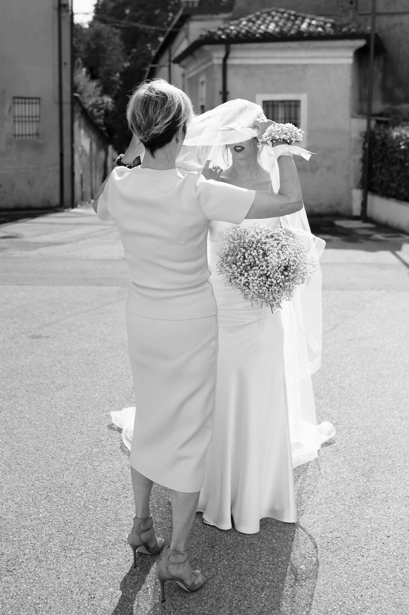 Black and white photo of two elegantly dressed figures on a street with flowing wedding dress details.