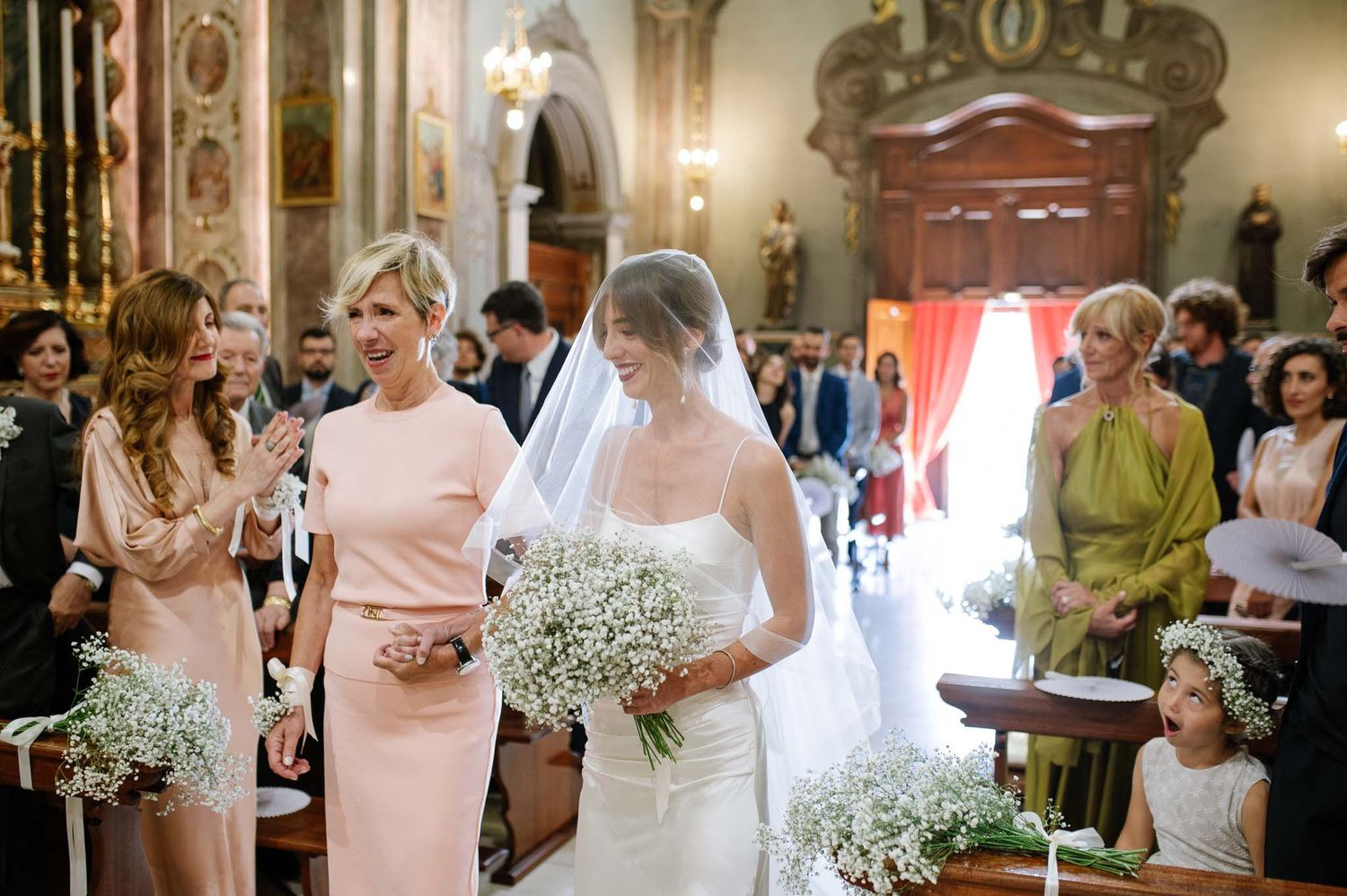 Wedding ceremony guests and floral decorations fill a traditional church interior.